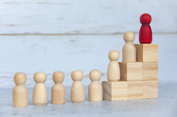 Wooden people figures on top of wooden blocks with red figure leading the rest. Business concept