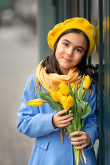 Portrait of a happy girl with a bouquet of yellow tulips on a walk in spring. Flowers for International Women's Day.