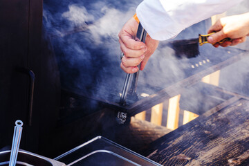 The process of cleaning the grill grate with a metal brush. The cook washes equipment for cooking on fire and coals. Unrecognizable person. selective focus