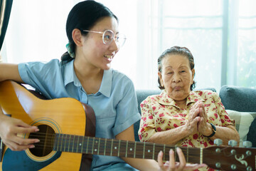 Asian elder woman playing an acoustic guitar.