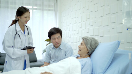 Senior Asian female patient resting on the medical bed in hospital and talking to her son. 
