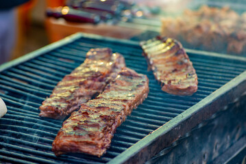 Barbecue ribs. Man in gloves flips grilled ribs on a charcoal grill. Picnic in the backyard during a family holiday. BBQ meat.