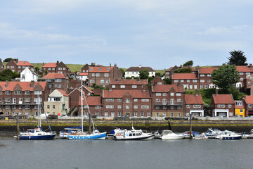 Obraz premium LANDSCAPE OF WHITBY ,THE SEASIDE TOWN OF NORTH YORKSHIRE.THE BRITISH HOUSES STYLE FROM BROWN BRICK WALL AND WHITE WINDOWS AND FISHING BOATS ,SPEED BOATS IN THE RIVER ERK