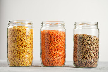 Three tall glass jars with dry red, yellow and green lentils on white background