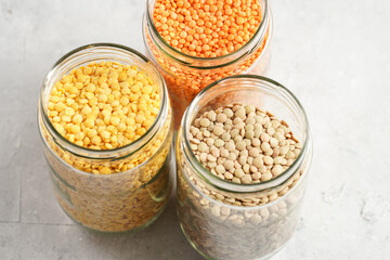 Three tall glass jars with dry red, yellow and green lentils on white background, top view
