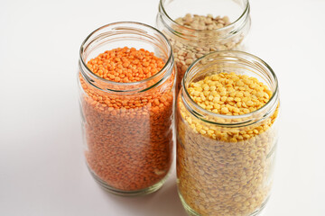 Three tall glass jars with dry red, yellow and green lentils on white background, top view