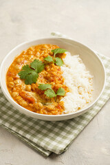 Indian red lentil curry with chickpeas, white rice and fresh cilantro - chana dal - in a white bowl on a green checkered kitchen towel