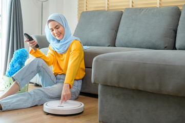 Young happy muslim woman relaxing and using smartphone in living room while Robotic vacuum cleaner working