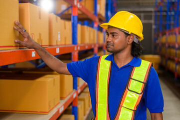 Young worker wearing helmet checking inventory and counting product on shelf in modern warehouse.