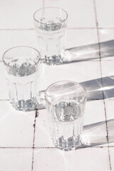 glass with clean clear water and sharp shadows stands. glass with water on white table on a tiled table