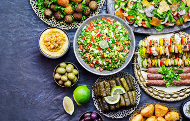 Arabic cuisine;Assorted of middle eastern traditional dishes. Stuffed vine leaves,olives, kibbeh, shish tawook, flafel, sambusak, tabbouleh and fattoush salad. Halal food. Top view with copy space. - obrazy, fototapety, plakaty