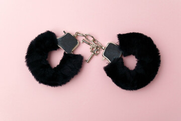 Black fluffy handcuffs. Erotic sex game with sexual bdsm toy. Pink background - obrazy, fototapety, plakaty