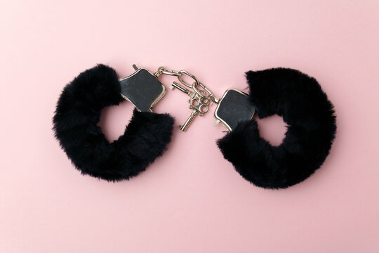 Black fluffy handcuffs. Erotic sex game with sexual bdsm toy. Pink background