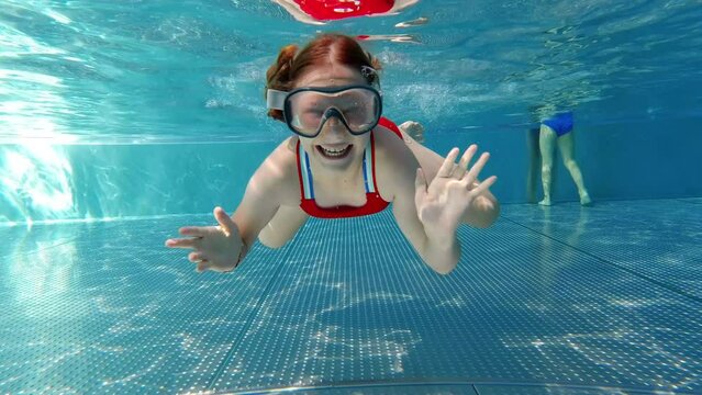 Happy child girl swimmimg and diving underwater in blue swimmimg pool at sunny day