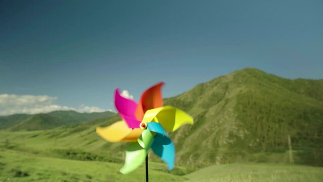 Mmulti-colored pinwheel close-up is spinning by force of the wind in background of green mountains