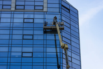 Glass façade repair and maintenance at high altitude. A worker stands in a lift at a high height and repairs the glass facade of the building.