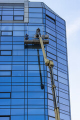 Glass façade repair and maintenance at high altitude. Workers stand in a lift at a great height and repair the glass facade of the building.