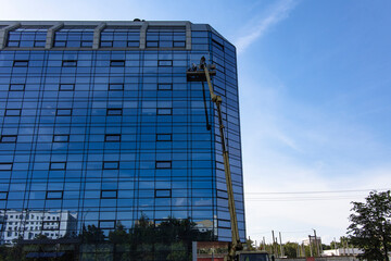 Glass façade repair and maintenance at high altitude. Workers stand in a lift at a great height and repair the glass facade of the building.