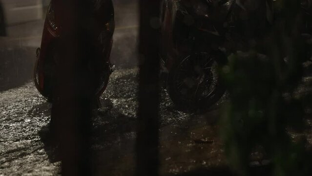 Slow Motion rain scenes during heavy thunder storm with close up of flooded sidwalk and bike wheels- and crossing cars passes behind- Koh Samui island in Thailand