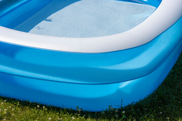 Close-up of a blue inflatable pool filled with clean cool water stands on the grass in the hot summer