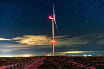 Night photo of a windmill and stars with abstract lighting. Wind turbine at night against the background of stars. Environment and Renewable Energy © alexmina