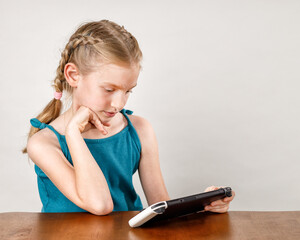 Little girl playing a game on console while sitting at the table with white background