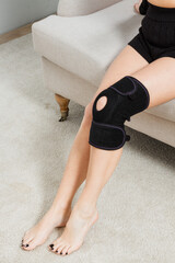 Black knee support brace on a woman leg. girl in an orthosis in the interior of the house....