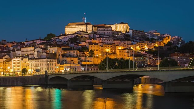 Day to night time lapse view of the historic old town of Coimbra seen from the Mondego River in Coimbra, Portugal, zoom in. 