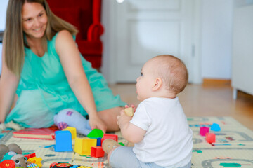 Baby boy and his mother sitting on the floor, having fun with toys