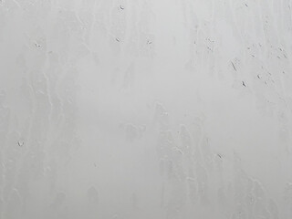 Weeping window in rainy, cloudy weather outside on street. Close up. Raindrops streaming down window. It's raining. Texture of window glass with streaks.