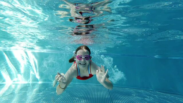 Slow motion video of diving little girl making bubbles underwater in swimming pool