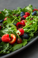 Delicious light salad of arugula and fresh sweet berries, black and red cherries and gooseberries, blueberries and raspberries