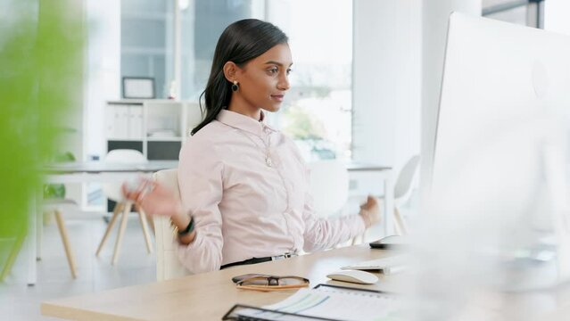 Young business woman stretching before typing an email on a desktop computer alone in an office at work. One Indian female corporate worker taking a break before finishing a deadline on a pc