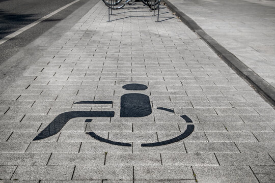 graue Pflastersteine am Stra&szlig;enrand mit schwarzem Symbol eines Rollstuhls f&uuml;r Behindertenparkfl&auml;che