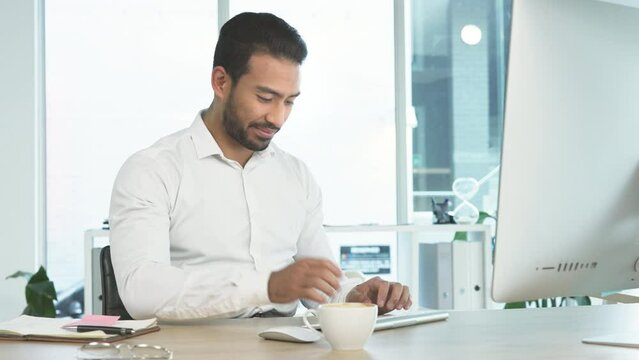 Business man working on a computer and drinking coffee in an office. Confident and ambitious entrepreneur typing emails and compiling online reports. Doing research and planning in a startup company