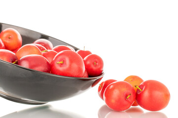 Several ripe juicy cherry plums in a black ceramic plate, close-up, isolated on a white background.