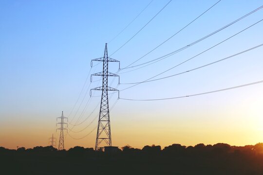 Silueta de torres de alta tensión para la conducción de electricidad. Imagen tomada al atardecer con los últimos rayos del sol al ponerse este en el horizonte. Madrid, España.