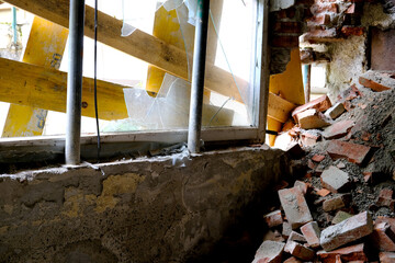 ruined room in abandoned building with broken windows without glass, basement air raid shelter, pile of bricks lying around, concept of destruction of buildings from bombing and rocket attacks