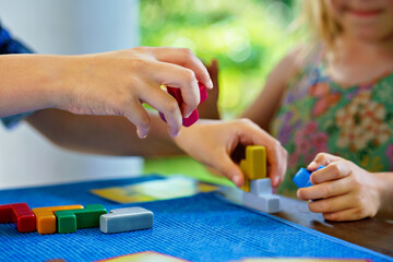 Children playing board game with colorful bricks. Closeup of hands build tower of wooden blocks, developing fine motor skills, home joint games. Leisure activities for children at home.