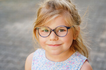 Portrait of a cute preschool girl with eye glasses outdoors. Happy funny child wearing blue...