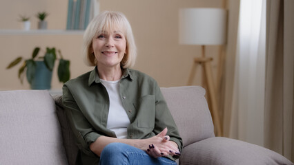 Portrait at home pensive thinking smiling beautiful older adult Caucasian lady looking away at window dreaming turning to camera sit on sofa senior retired woman grandma feel satisfied in living room