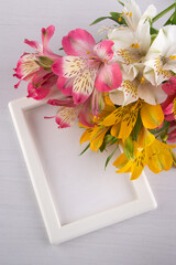 Flat lay of beautiful flowers on white background on corners of photoframe with space for your text. Vertical photo, top view. Tender pink, yellow lilly flowers