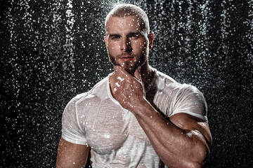Fototapeta na wymiar Muscular man under the rain in studio. Sexy male in water drops