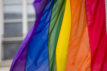 Close Up rainbow gay pride flag outside on a street. Symbol of the Lesbian Bisexual Transgender LGBT community waving in wind against cloudy sky. Social movement for freedom and equliaty. Copy Space