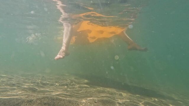 Underwater view of a female legs hanging down from a lilo while floating on the beautiful Harrison Lake surrounded with mountains in Harrison Hot Springs