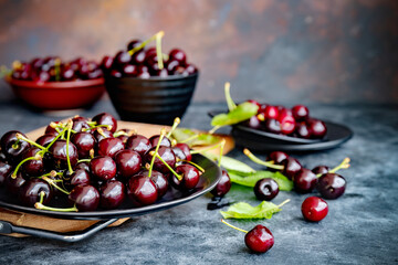 Close-up of fresh black cherry with leaves on grey ceramic plate on dark background. Dark low key photo. Selective focus. Blurred background.