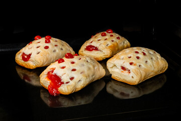 Four baked puff pastry buns with red strawberry jam on tray in electric oven, black background. Homemade bakery, food, cooking and pastry concept