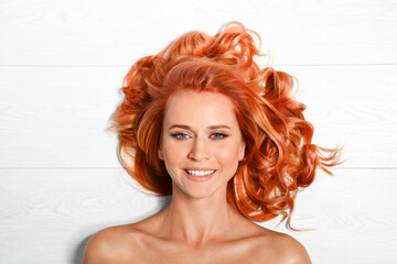 Beautiful woman with long orange hair on white wooden background, top view