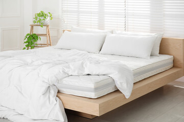 Fototapeta na wymiar Wooden bed with soft white mattress, blanket and pillows in cozy room interior