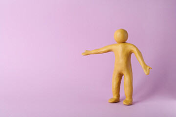 Human figure with arms wide open made of yellow plasticine on violet background. Space for text